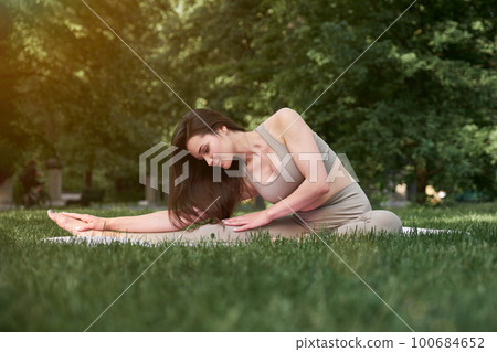 A young woman with a slim figure and long hair goes in for sports in the park on a warm summer day. A young woman with a slim figure and long hair goes in for sports in the park on a warm summer day. 100684652