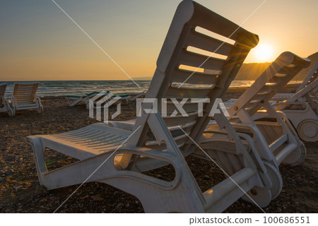White sunbeds in a sandy beach at sunset White sunbeds in a sandy beach at sunset 100686551