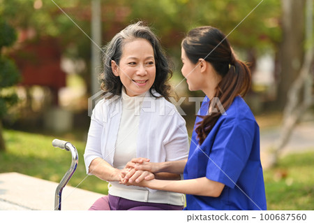 Young female caregiver talking with senior woman, sitting at nursing home park. Assistance and rehabilitation concept Young female caregiver talking with senior woman, sitting at nursing home park. Assistance and rehabilitation concept 100687560
