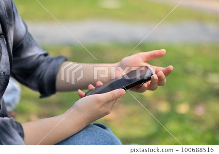 Cropped side view image of a woman in flannel shirt using her phone in the park. Cropped side view image of a woman in flannel shirt using her phone in the park. 100688516
