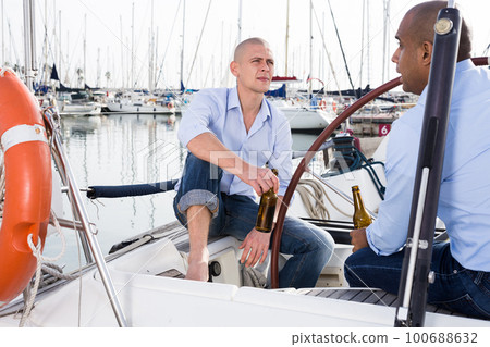 A couple of guys in blue shirts and jeans chatting on a private yacht in port 100688632