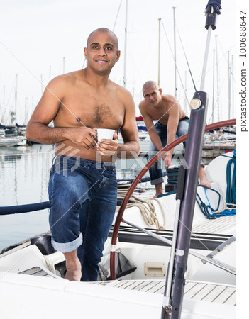 Latin American topless with a cup of coffee in his hand standing on the deck of a yacht in the seaport 100688647