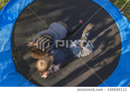 children look at the phone while lying on a trampoline children look at the phone while lying on a trampoline 100689112