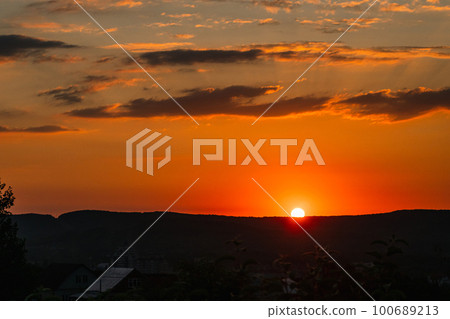 A beautiful yellow-orange sunset. Clouds hang motionless in the sky. You can see the silhouette of a tree in the foreground. The sun is about to set behind the mountain. A beautiful yellow-orange sunset. Clouds hang motionless in the sky. You can see the silhouette of a tree in the foreground. The sun is about to set behind the mountain. 100689213