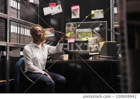 Private detective using augmented reality technology for clues analysis. African american woman investigator making hand gesture and pointing with finger while working in ar Private detective using augmented reality technology for clues analysis. African american woman investigator making hand gesture and pointing with finger while working in ar 100689942