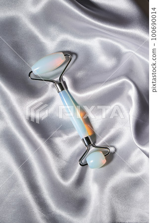 Blue jade face roller and Gua Sha scraping for beauty facial massage therapy on silver textured silk background. Blue jade face roller and Gua Sha scraping for beauty facial massage therapy on silver textured silk background. 100690014