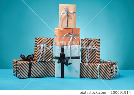 Different sizes, colorful, striped and plain paper gift boxes tied with ribbons and bows on a blue surface and background. Close-up, copy space. 100691914