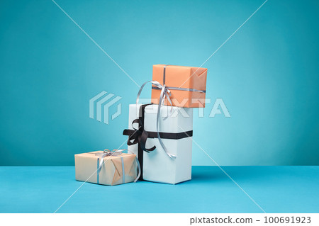 Different sizes, colorful, striped and plain paper gift boxes tied with ribbons and bows on a blue surface and background. Close-up, copy space. 100691923