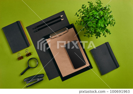 Top view in focus with different office equipment, supplies, stationery. Green background with copy space. Education, workplace concept. Close-up. 100691963