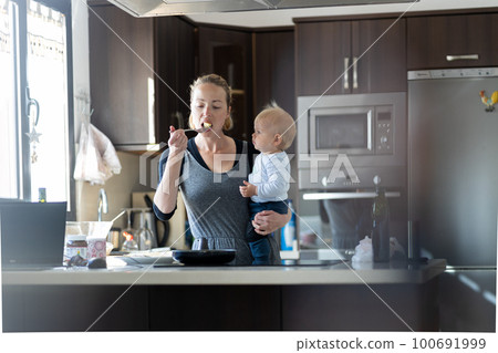 Happy mother and little infant baby boy prepering healthy breakfast together in domestic kitchen. Family, lifestyle, domestic life, food, healthy eating and people concept 100691999