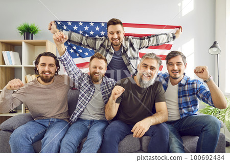 Group of Americans with flag sitting on sofa and watching soccer match on television 100692484