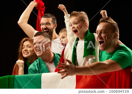 Excited people standing with flag of country. Football, soccer fans emotionally cheering up favourite team during match. Men visiting game with kids 100694539