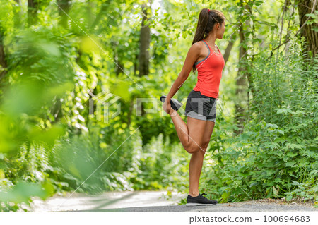 Fit stretch woman stretching quad leg muscle standing getting ready to run jogging outside in summer nature forest park green trees background. Fitness runner athlete running girl Fit stretch woman stretching quad leg muscle standing getting ready to run jogging outside in summer nature forest park green trees background. Fitness runner athlete running girl 100694683