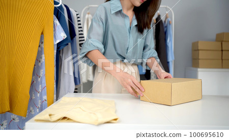 Beautiful Asian woman packing a postal package on the table, online shopping and e-commerce in small start up business concept. 100695610