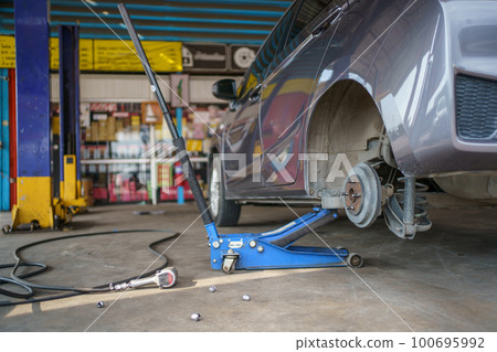 Technician or repairman using a hydraulic jack lift up a car at rear wheel to changing a flat tyre. Technician or repairman using a hydraulic jack lift up a car at rear wheel to changing a flat tyre. 100695992