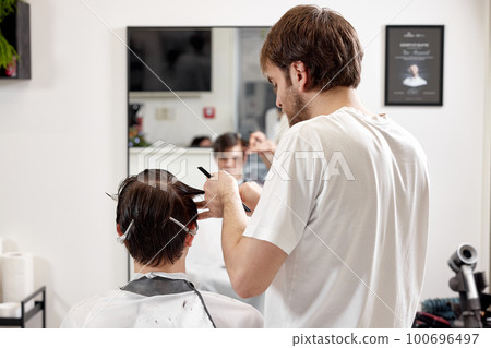young caucasian man getting haircut by professional male hairstylist young caucasian man getting haircut by professional male hairstylist 100696497