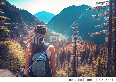 Traveler girl with a backpack looks at a beautiful landscape space: a mountain gorge framed by a coniferous forest. A concept for travel and a sense of the spirit of adventure and freedom. 100696871