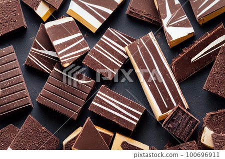 Textured background with square and rectangular pieces of chocolate or sweet candies scattered chaotically on a table. Various shapes and textures of the candies and visually appealing composition Textured background with square and rectangular pieces of chocolate or sweet candies scattered chaotically on a table. Various shapes and textures of the candies and visually appealing composition 100696911