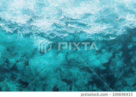 Top-down view of a turquoise sea with a textured background. The water is transparent enough to reveal the relief and structure of the ocean floor, evoking the idea of diving or a sea journey 100696915