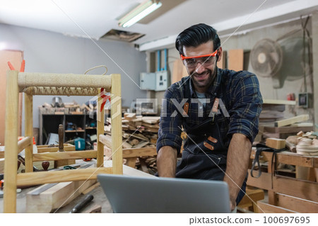 young carpenter caucasian man with laptop make drawing on wood to design at workspace. young carpenter caucasian man with laptop make drawing on wood to design at workspace. 100697695