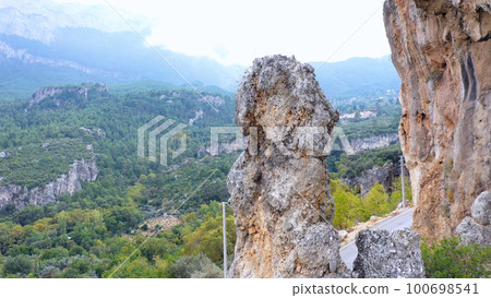 Rocky cliff on the background of green mountain valley. Scenic rocky formation over country road. Tourism and adventures concept. Rocky cliff on the background of green mountain valley. Scenic rocky formation over country road. Tourism and adventures concept. 100698541