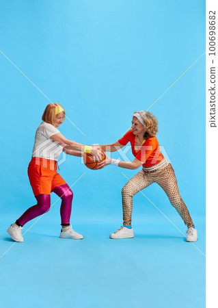 Elderly sportive woman in colorful uniform training, posing, competing for basketball bal against blue studio background. Concept of sport and health 100698682