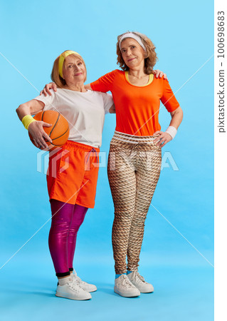Elderly sportive woman in colorful uniform posing with basketball ball against blue studio background. Concept of sport and health 100698683