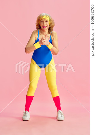Showing strength. Senior old woman in colorful sportswear training, posing against pink studio background. Concept of sport and health care 100698706