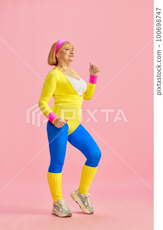 Fitness lover. Senior, aged, sporty woman in colorful sportswear training, posing against pink studio background. Concept of sport and health care 100698747