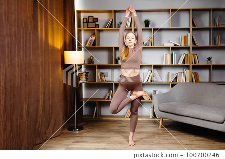 Finding right balance. Woman doing perfect tree pose in room next to the window, free space Finding right balance. Woman doing perfect tree pose in room next to the window, free space 100700246