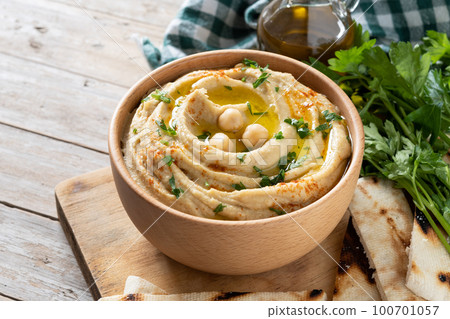 Chickpea hummus in a wooden bowl garnished with parsley, paprika and olive oil isolated on white background 100701057