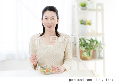 Middle-aged woman eating salad in the living room 100701725