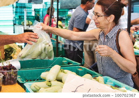 A middle-aged white Caucasian woman at an open-air food market buying a bag of vegetables 100702367