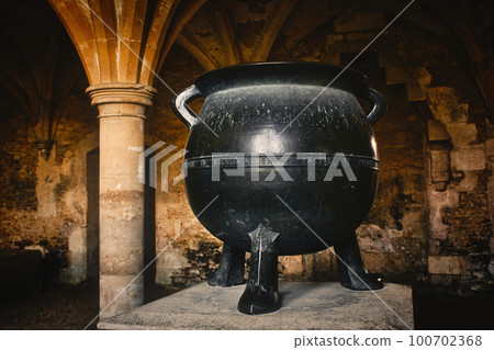A big black cast iron metal cauldron in a medieval castle basement under an arch A big black cast iron metal cauldron in a medieval castle basement under an arch 100702368