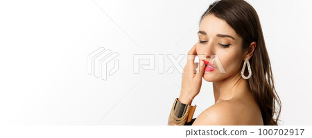 Fashion and beauty concept. Tender and feminine brunette woman touching red lips and looking down sensually, standing over white background Fashion and beauty concept. Tender and feminine brunette woman touching red lips and looking down sensually, standing over white background 100702917