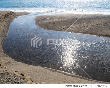 A river flowing along the sandy beach. 100702987