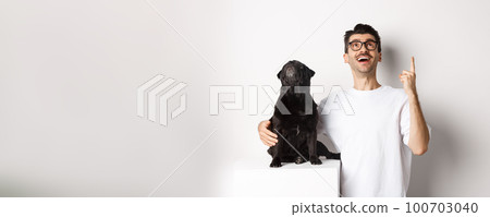 Image of happy young man and dog both looking up at promo, owner pointing finger at top, pug staring at loog, standing over white background 100703040