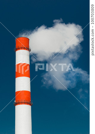 Pollution of the environment, ecology and air. Withdrawal of combustion products of soot, smoke and gases from the pipe of an industrial plant into the atmosphere against the background of a blue sky 100703809