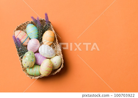 Colorful Easter eggs in wicker basket against colored background, closeup. top view with copy space 100703922