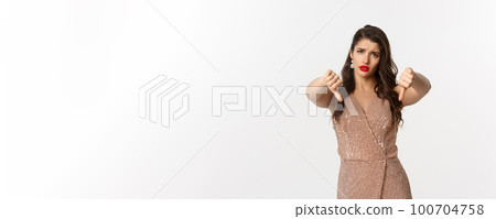 Concept of celebration, holidays and party. Displeased young woman in elegant dress showing thumbs-down, dislike and disapprove something, complaining Concept of celebration, holidays and party. Displeased young woman in elegant dress showing thumbs-down, dislike and disapprove something, complaining 100704758