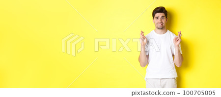 Nervous guy crossing fingers for good luck, hoping for something, standing over yellow background Nervous guy crossing fingers for good luck, hoping for something, standing over yellow background 100705005