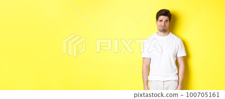 Disappointed guy looking upset, sulking and frowning, standing displeased against yellow background Disappointed guy looking upset, sulking and frowning, standing displeased against yellow background 100705161