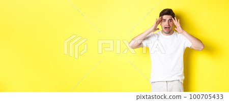 Frustrated guy looking shocked, panicking and holding hands on head, standing against yellow background Frustrated guy looking shocked, panicking and holding hands on head, standing against yellow background 100705433