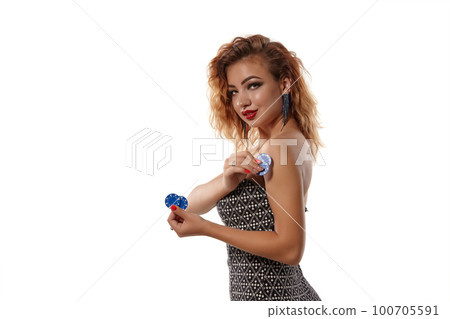 Ginger girl wearing gray dress is posing holding blue chips in her hands standing isolated on white background. Casino, poker. Close-up shot. Ginger girl wearing gray dress is posing holding blue chips in her hands standing isolated on white background. Casino, poker. Close-up shot. 100705591