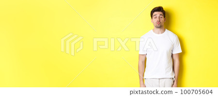 Image of lovely man close eyes and pucker lips, waiting for kiss, standing in white clothes against yellow background 100705604