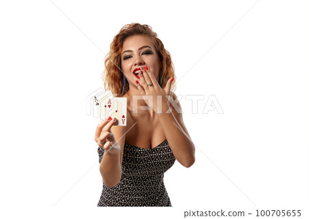Ginger girl wearing gray dress is posing holding two playing cards in her hands standing isolated on white background. Casino, poker. Close-up shot. Ginger girl wearing gray dress is posing holding two playing cards in her hands standing isolated on white background. Casino, poker. Close-up shot. 100705655