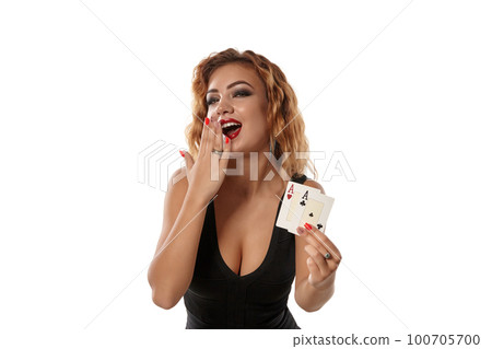 Ginger girl wearing a black dress is posing holding two playing cards in her hands standing isolated on white background. Casino, poker. Close-up. 100705700