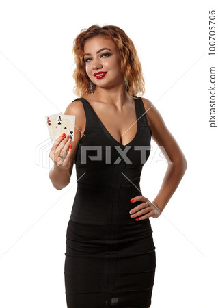 Ginger girl wearing a black dress is posing holding two playing cards in her hands standing isolated on white background. Casino, poker. Close-up. 100705706