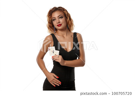 Ginger girl wearing a black dress is posing holding two playing cards in her hands standing isolated on white background. Casino, poker. Close-up. Ginger girl wearing a black dress is posing holding two playing cards in her hands standing isolated on white background. Casino, poker. Close-up. 100705720