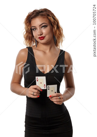 Ginger girl wearing a black dress is posing holding two playing cards in her hands standing isolated on white background. Casino, poker. Close-up. Ginger girl wearing a black dress is posing holding two playing cards in her hands standing isolated on white background. Casino, poker. Close-up. 100705724